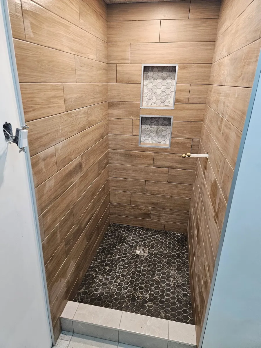 Douche en céramique imitation bois avec deux niches superposées en mosaïque hexagonale, encadrées d'un profilé métallique