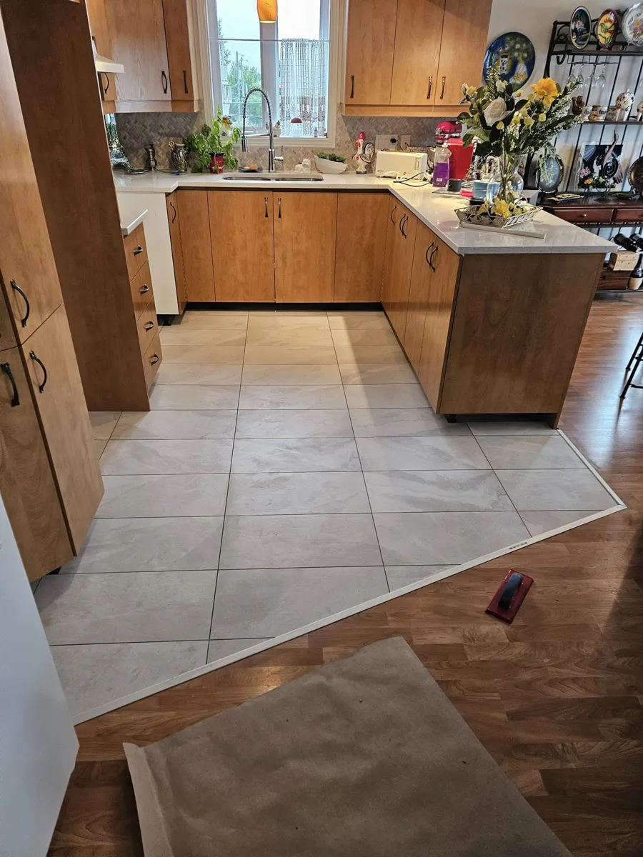 Plancher de cuisine en céramique autour de l'îlot, avec une transition nette vers le bois franc de la salle à manger