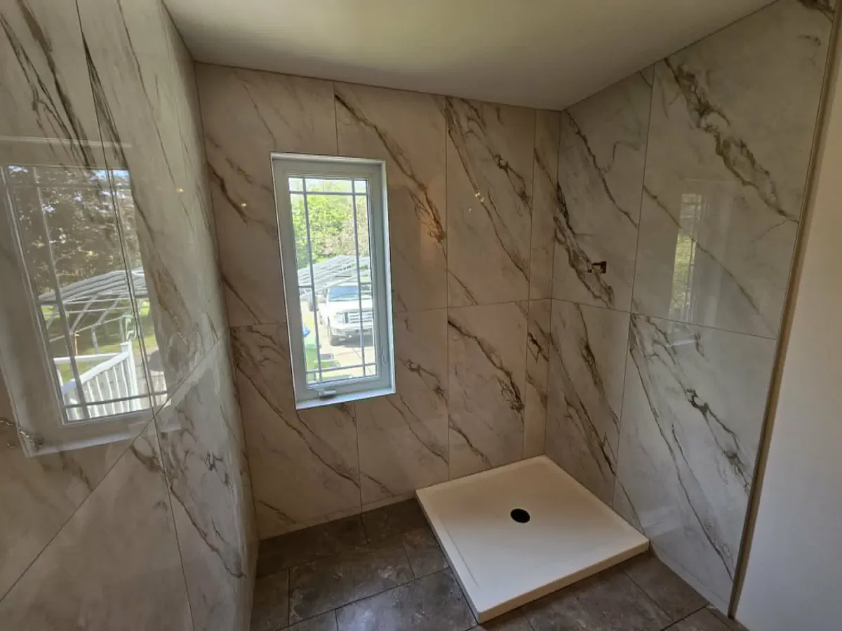 Douche habillée de grand format effet marbre blanc veiné de gris et d'or, avec la fenêtre encadrée de céramique
