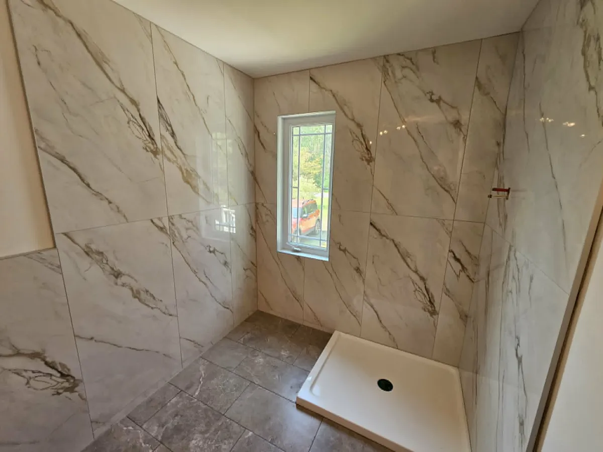 Murs de douche en grand format effet marbre, coupes ajustées autour de la fenêtre et au pied de la base de douche