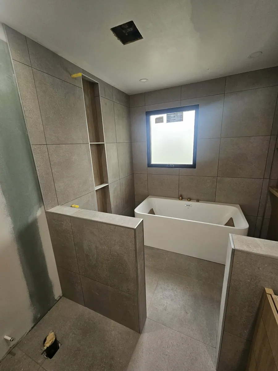 Vue d'ensemble de la salle de bain : murets de séparation, bain autoportant et mur de céramique jusqu'au plafond autour de la fenêtre