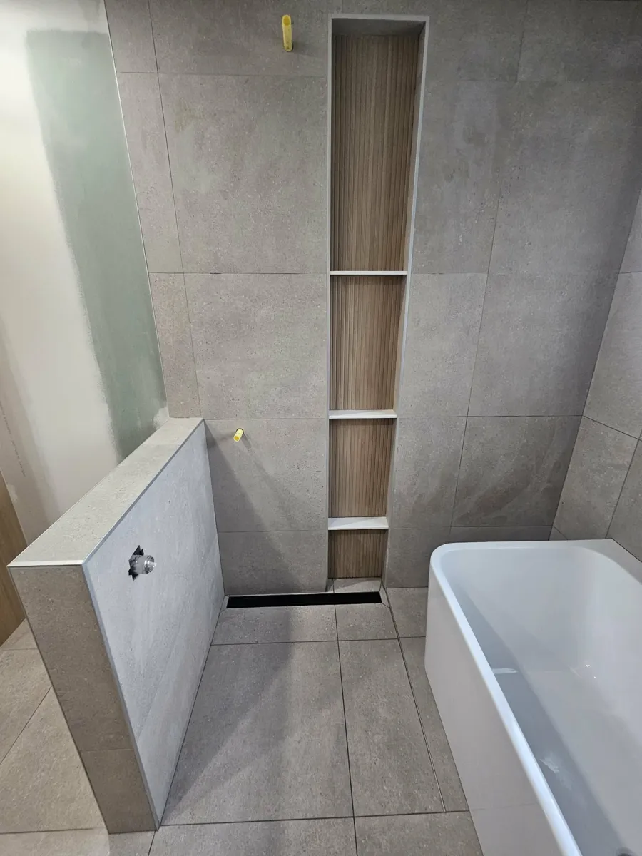 Douche à l'italienne avec drain linéaire au pied du mur et niche verticale pleine hauteur à fond aspect bois